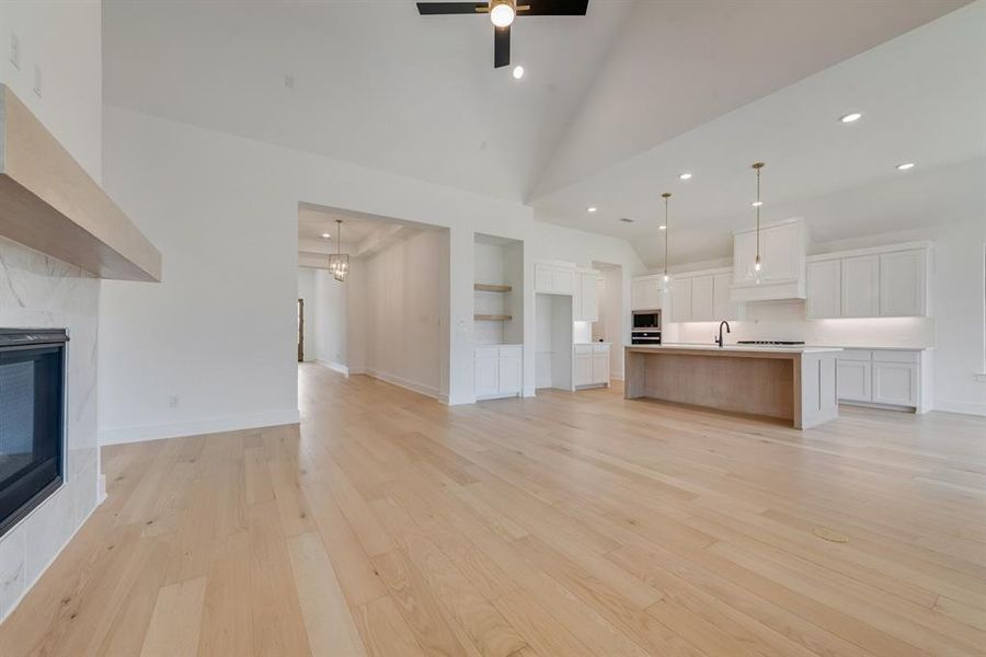 Unfurnished living room featuring a premium fireplace, light wood-type flooring, high vaulted ceiling, and recessed lighting