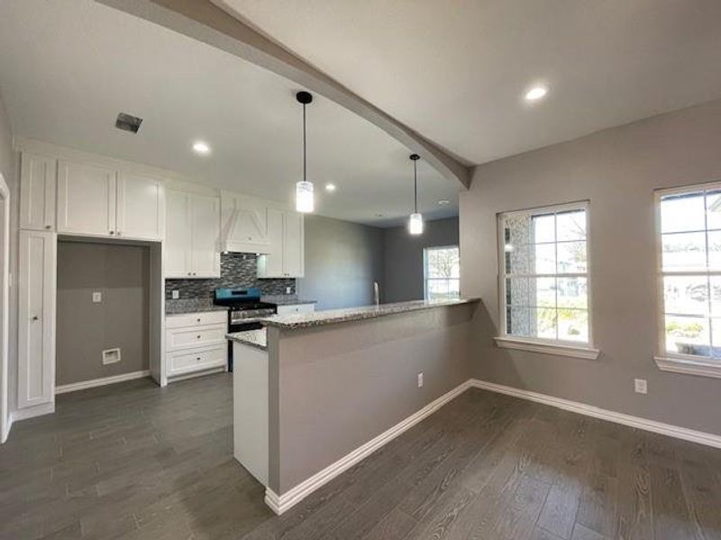 Looking in kitchen featuring stainless steel gas range, wood-style flooring, white cabinets, and tasteful backsplash Looking in kitchen featuring stainless steel gas range, wood-style flooring, white cabinets, and tasteful backsplash