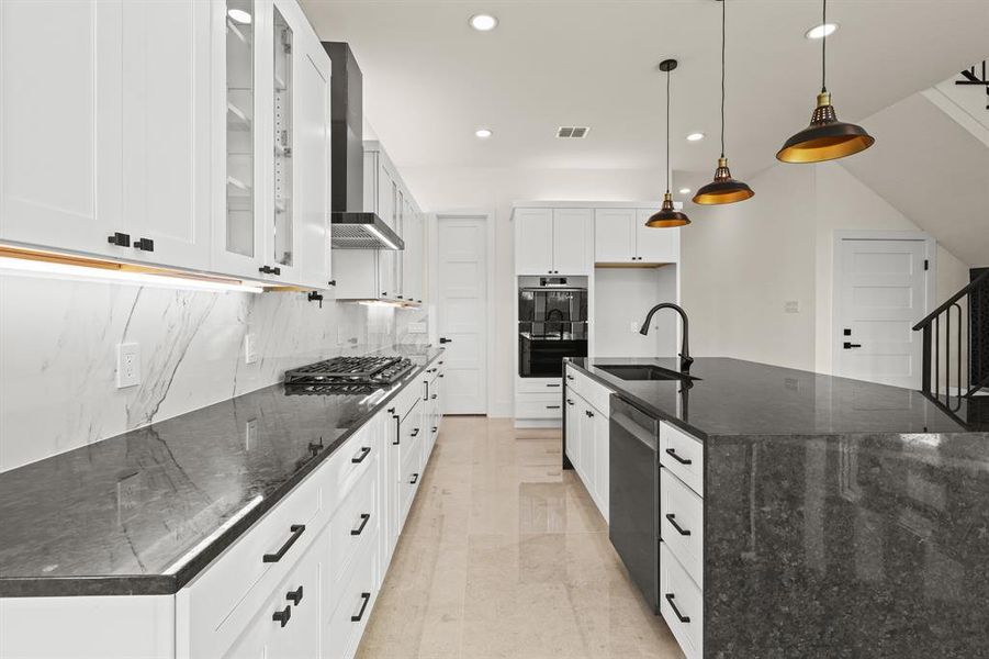 Kitchen with appliances with stainless steel finishes, pendant lighting, white cabinets, and a spacious island