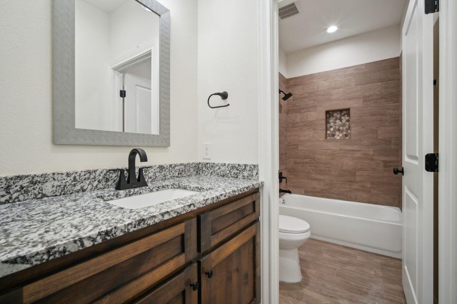 Full bathroom featuring toilet, vanity, wood finished floors, washtub / shower combination, and visible vents Full bathroom featuring toilet, vanity, wood finished floors, washtub / shower combination, and visible vents