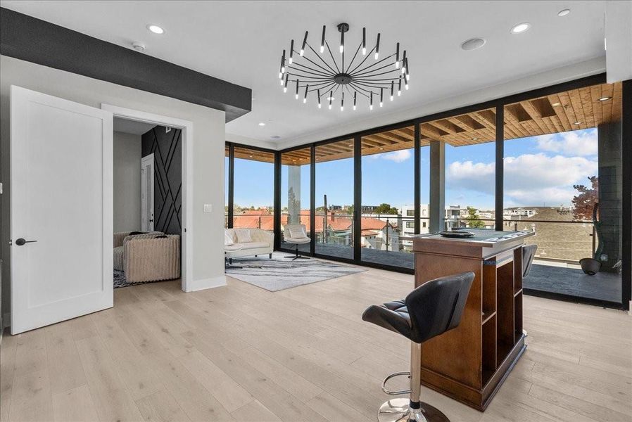 This room features modern design with floor-to-ceiling windows offering expansive city views. It includes a stylish chandelier, light wood flooring, and access to a covered balcony. Perfect for a home office or lounge area. This room features modern design with floor-to-ceiling windows offering expansive city views. It includes a stylish chandelier, light wood flooring, and access to a covered balcony. Perfect for a home office or lounge area.