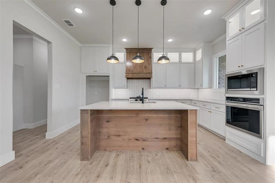 Kitchen featuring crown molding, glass fronted cabinets, white cabinetry, stainless steel appliances, and decorative light fixtures