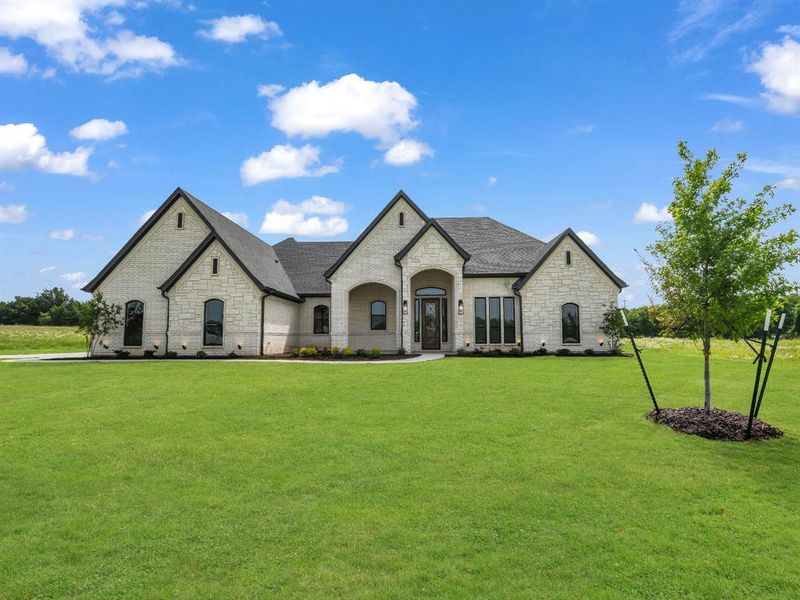 French country style house with a front yard, stone siding, and a shingled roof French country style house with a front yard, stone siding, and a shingled roof