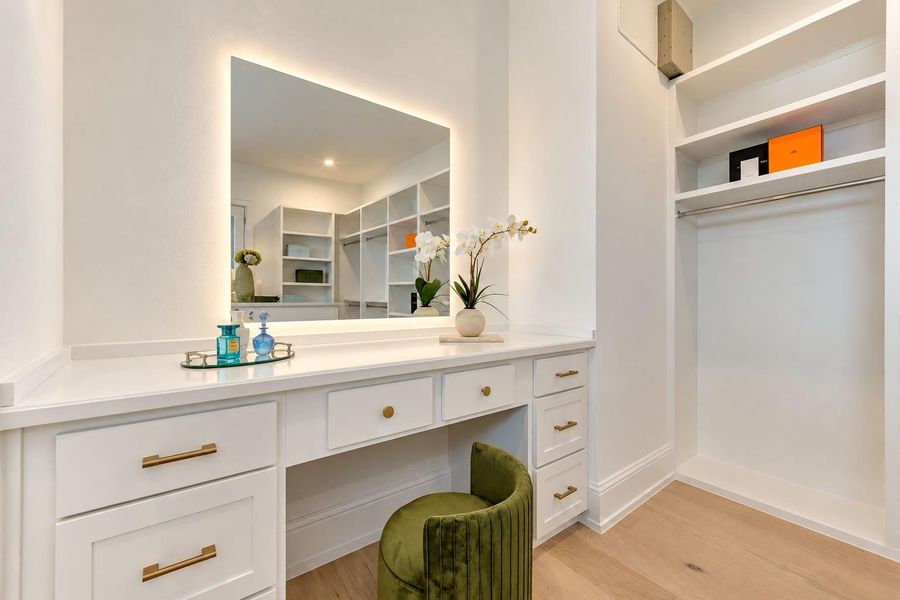 Elegant dressing area within the primary closet featuring a built-in vanity, custom cabinetry, illuminated statement mirror, and dedicated display shelving. Thoughtfully designed for getting ready in style, this sophisticated space adds a boutique-inspired finishing touch to the primary suite. Elegant dressing area within the primary closet featuring a built-in vanity, custom cabinetry, illuminated statement mirror, and dedicated display shelving. Thoughtfully designed for getting ready in style, this sophisticated space adds a boutique-inspired finishing touch to the primary suite.