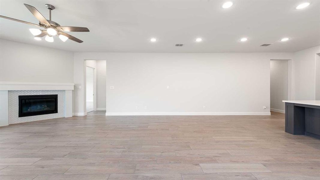 Unfurnished living room with a tiled fireplace, light wood-type flooring, and ceiling fan