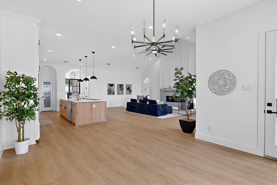 Living room featuring arched walkways, a chandelier, light wood-type flooring, a towering ceiling, and recessed lighting