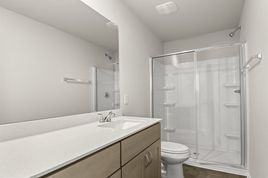 Image of a primary bathroom with light brown cabinets, white vanity, a large mirror and a white vinyl walk-in shower