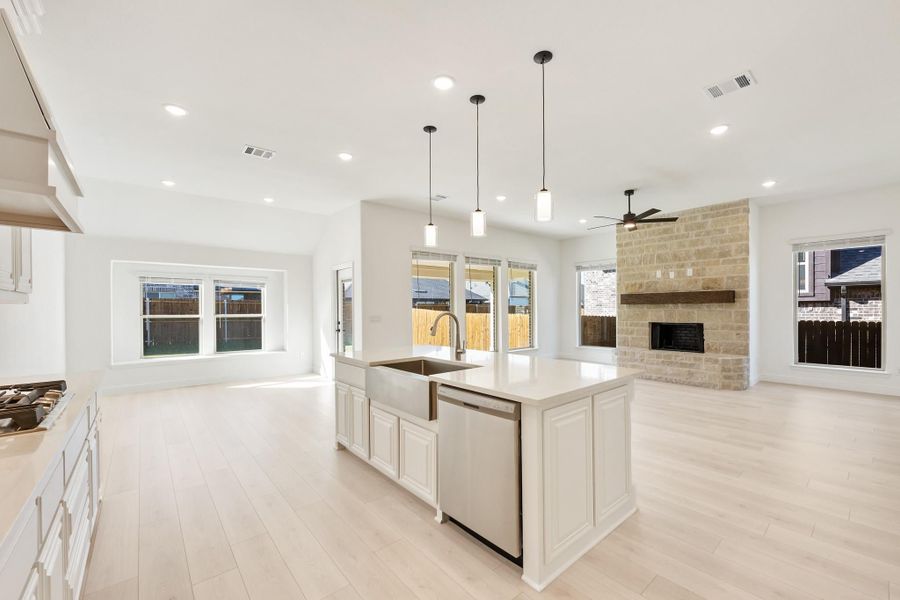 Open-concept kitchen with white island, pendant lights, and stone fireplace in adjoining living area Open-concept kitchen with white island, pendant lights, and stone fireplace in adjoining living area