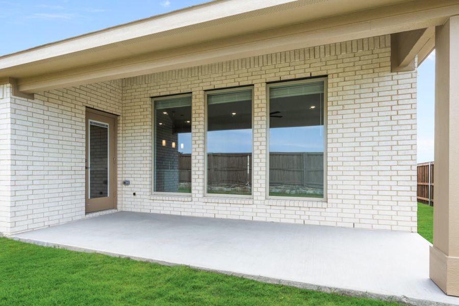 Covered back patio with concrete slab, white brick exterior, large windows, and green lawn