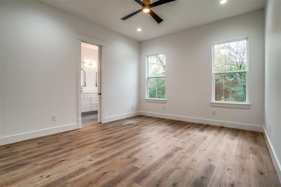 Unfurnished bedroom featuring ceiling fan, light wood-type flooring, multiple windows, and ensuite bath