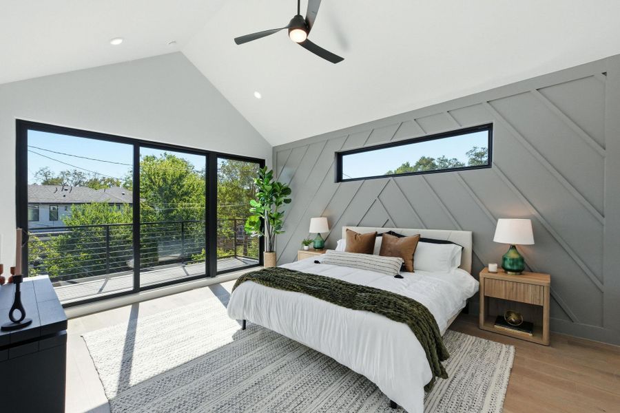 Bedroom featuring high vaulted ceiling, access to exterior, wood finished floors, a ceiling fan, and a decorative wall Bedroom featuring high vaulted ceiling, access to exterior, wood finished floors, a ceiling fan, and a decorative wall