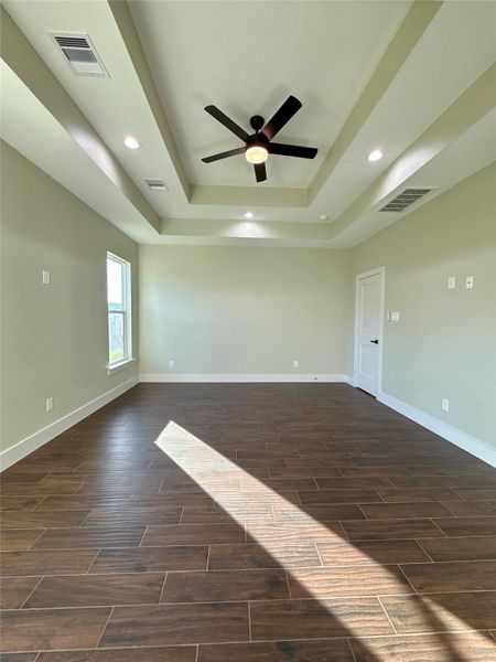 This spacious room features elegant wood-look tile flooring and a stylish tray ceiling with recessed lighting and a ceiling fan. Ample natural light flows through a large window, enhancing the room's inviting ambiance. This spacious room features elegant wood-look tile flooring and a stylish tray ceiling with recessed lighting and a ceiling fan. Ample natural light flows through a large window, enhancing the room's inviting ambiance.