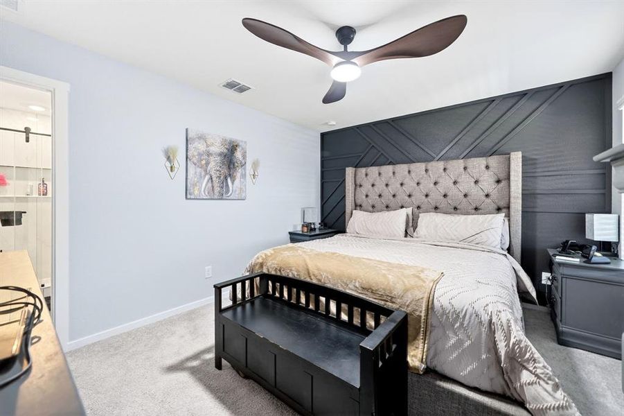 Bedroom featuring a dark accent wall with geometric molding, a ceiling fan with integrated lighting, and light-colored carpeting