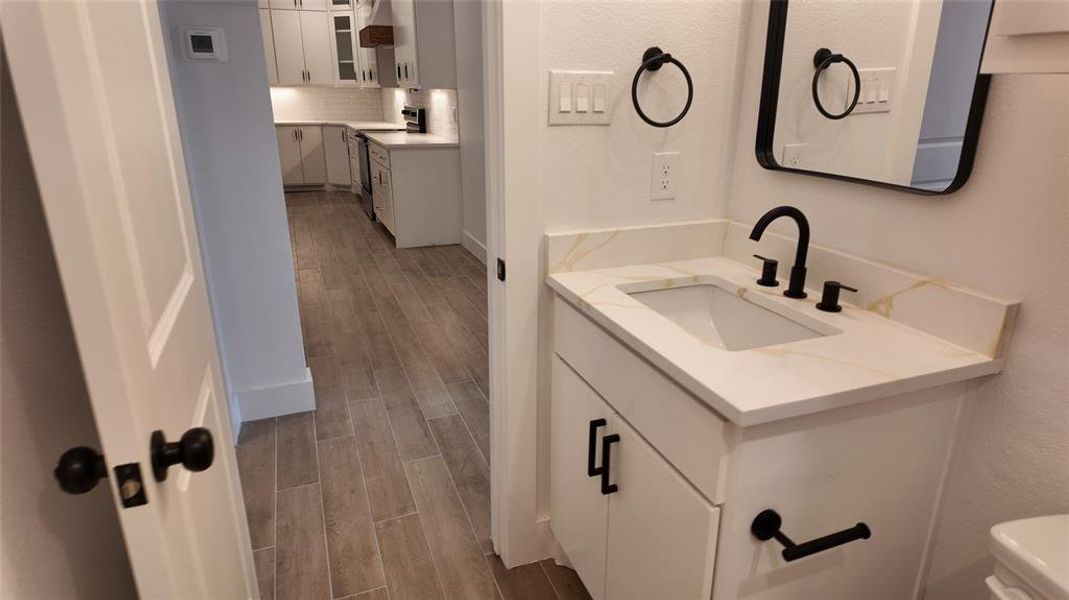 Half bath with wood finish floors, decorative backsplash, vanity, and a textured wall Half bath with wood finish floors, decorative backsplash, vanity, and a textured wall