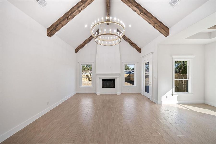 Unfurnished living room with high vaulted ceiling, plenty of natural light, light wood-style flooring, a large fireplace, and a chandelier