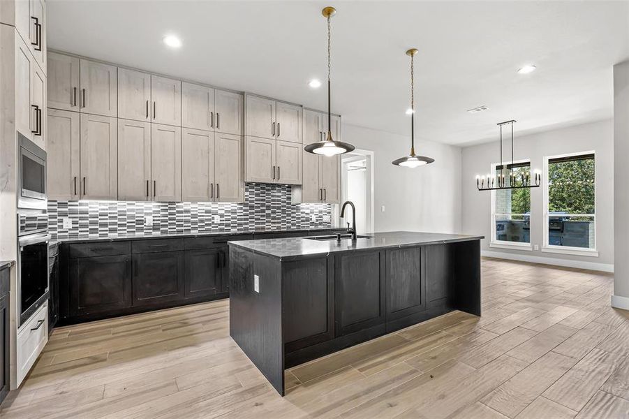 Kitchen with appliances with stainless steel finishes, pendant lighting, backsplash, an island with sink, and light wood-type flooring