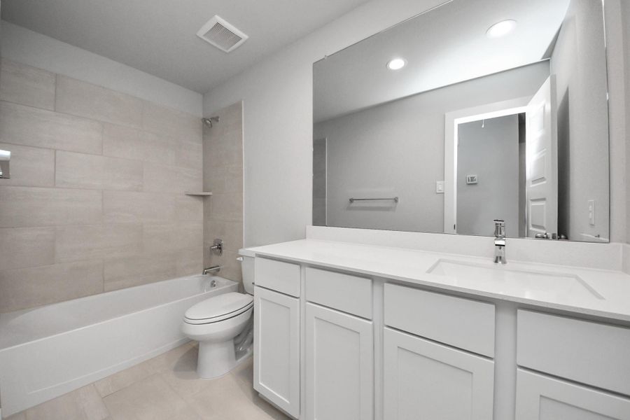 Secondary bath features tile flooring, bath/shower combo with tile surround, light stained wood cabinets, beautiful light countertop. Sample photo of completed home with similar floor plan. Actual colors and selections may vary.