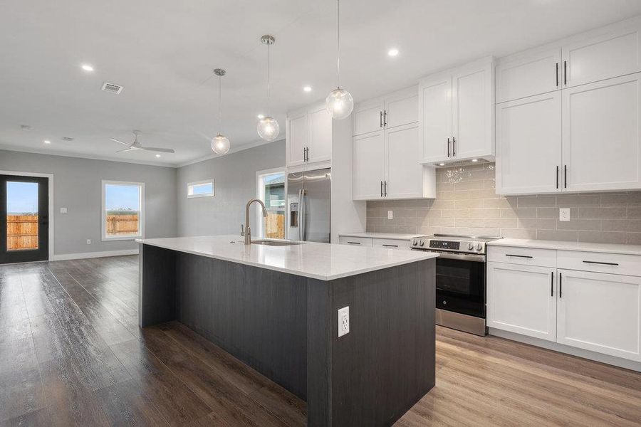 Two tone kitchen featuring stainless steel appliances, ceiling fan, an island with sink, pendant lighting, and light wood-type flooring