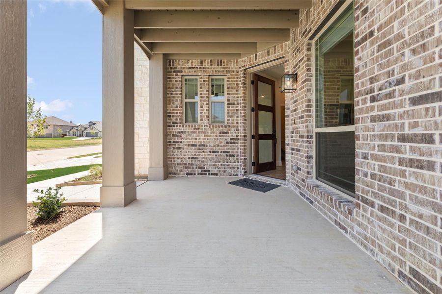 Covered front porch with brick exterior, wood front door, and concrete floor on a new home Covered front porch with brick exterior, wood front door, and concrete floor on a new home