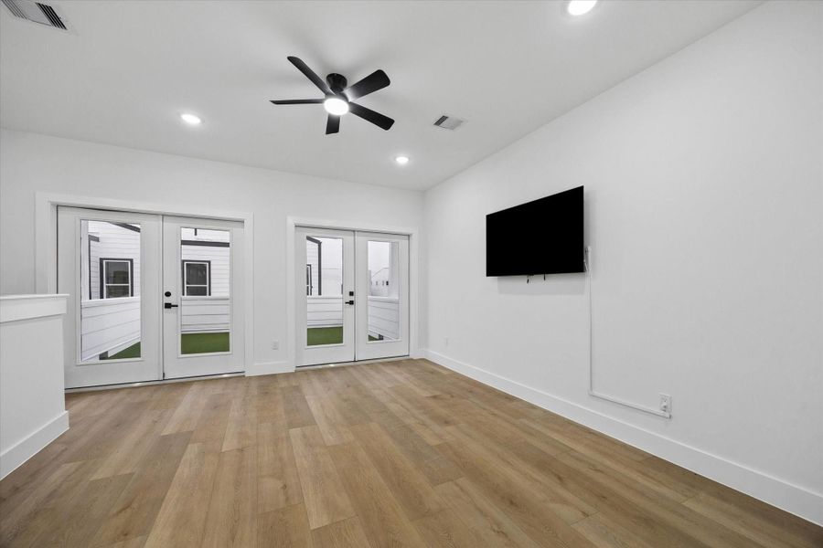 This room features sleek hardwood flooring, a ceiling fan, and ample natural light from double glass doors. It includes a wall-mounted TV and opens to a small outdoor area, offering a modern and airy space. This room features sleek hardwood flooring, a ceiling fan, and ample natural light from double glass doors. It includes a wall-mounted TV and opens to a small outdoor area, offering a modern and airy space.