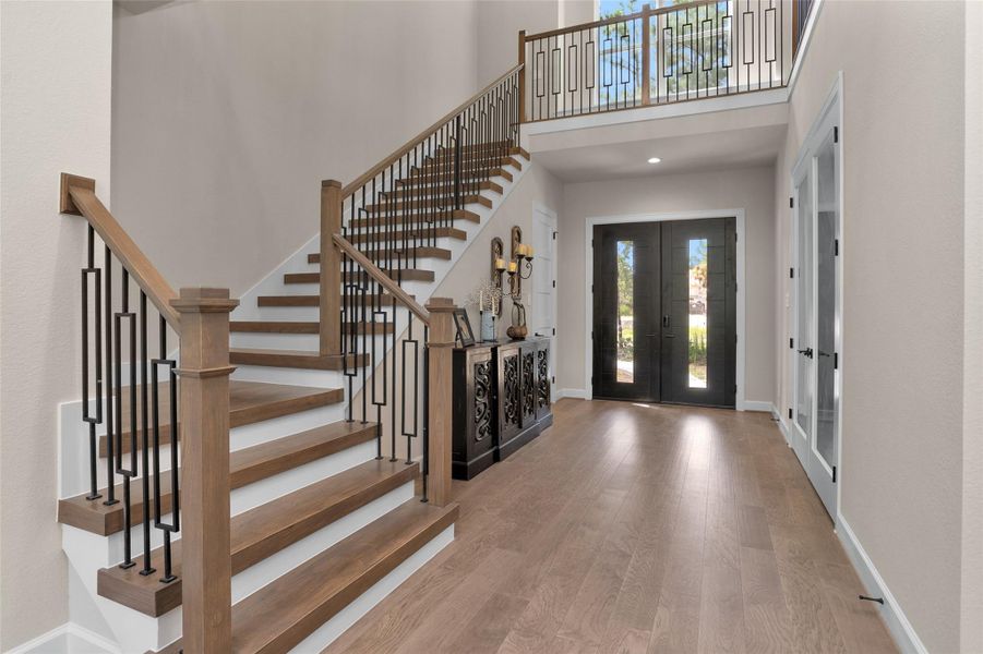 The grand entryway makes a bold first impression with double front doors, soaring ceilings and a statement staircase featuring wood treads and modern iron balusters—all anchored by rich hardwood floors.
