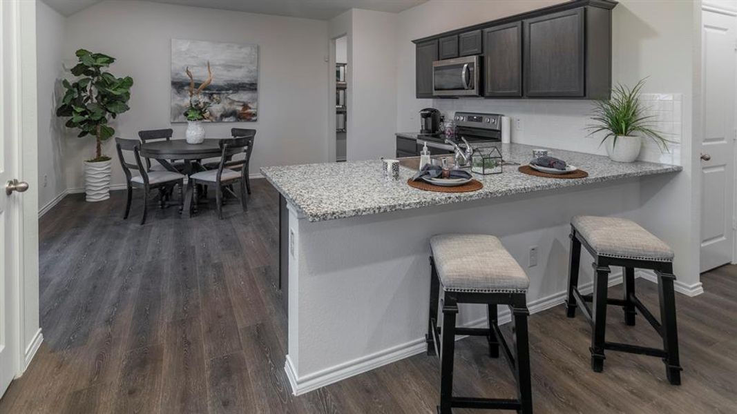 Kitchen featuring a breakfast bar area, a peninsula, stainless steel appliances, dark wood-type flooring, and light stone counters