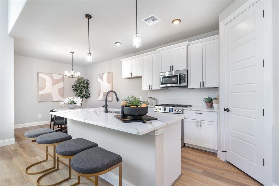 Kitchen with hanging light fixtures, a center island with sink, white cabinets, and stainless steel appliances