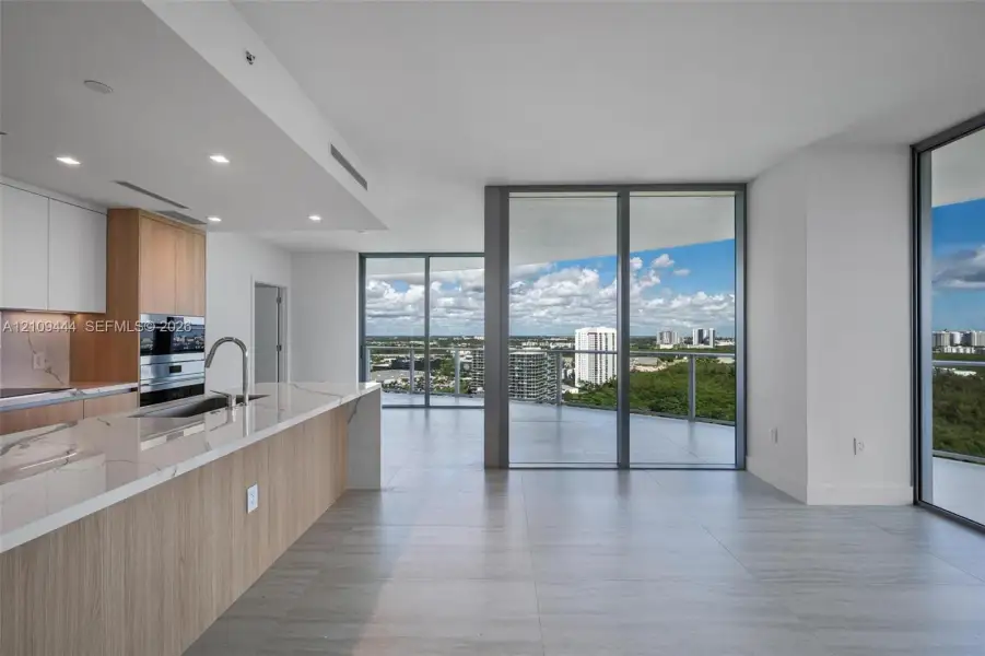 Kitchen featuring wood-finish cabinetry, stone countertops, built-in double ovens, and expansive floor-to-ceiling glass panel doors opening to a wrap-around balcony with exterior horizon scenery