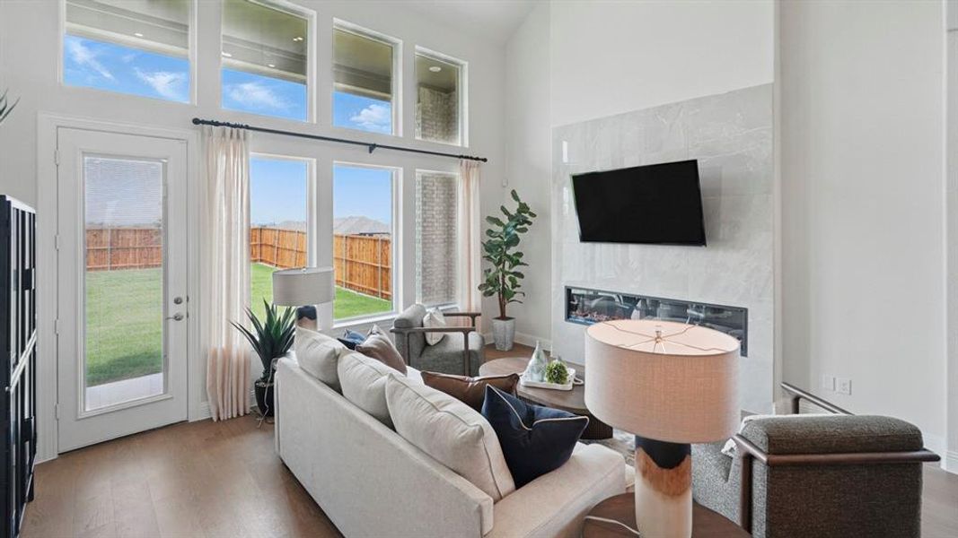 Two-story living area with wood-finish flooring, a contemporary fireplace featuring a stone-look surround, and a wall of windows including transom windows