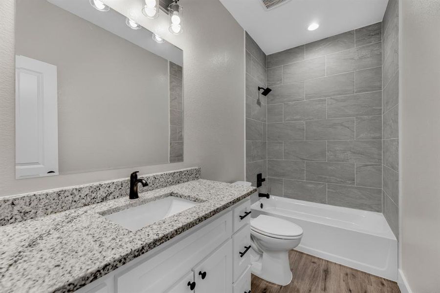 Full bathroom with tiled shower / bath combo, vanity, toilet, and wood-type flooring