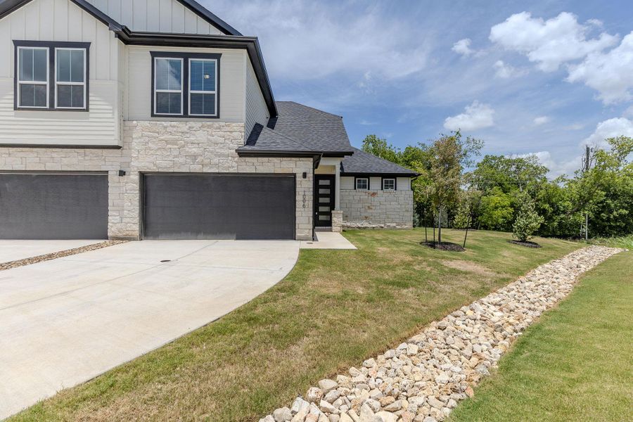 Modern stone and siding residence with two-car garage, featuring a verdant lawn and a natural rock drainage channel. Modern stone and siding residence with two-car garage, featuring a verdant lawn and a natural rock drainage channel.