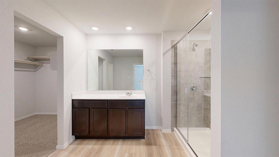 A well-appointed primary bathroom featuring a spacious walk-in closet and elegant wood flooring.