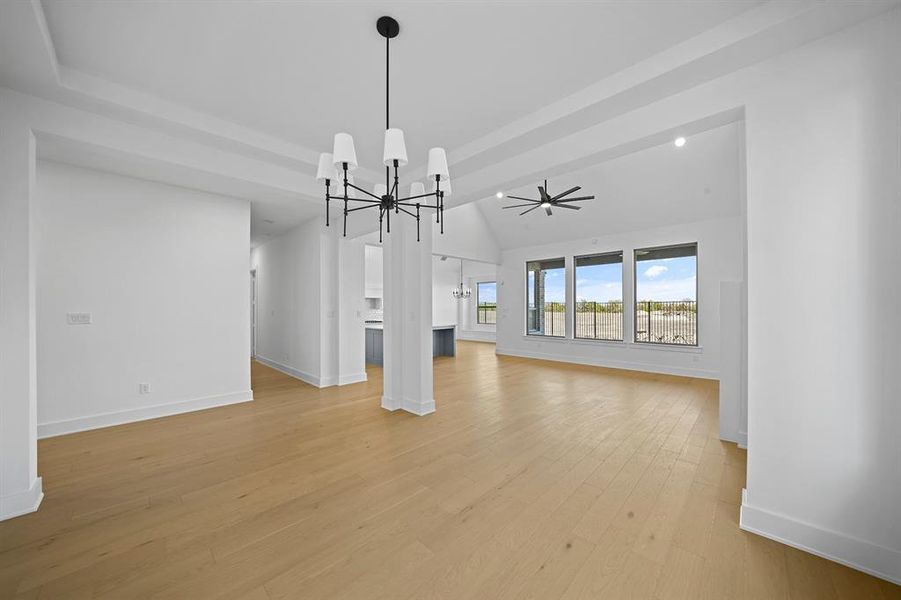 Unfurnished living room with a chandelier, light wood-style floors, vaulted ceiling, and a ceiling fan