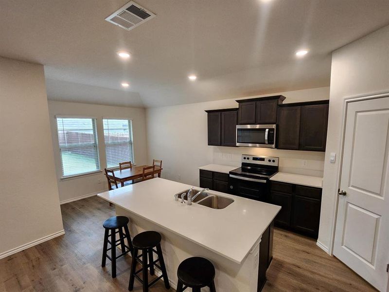 Kitchen featuring stove, dark wood-style floors, dark brown cabinets, a center island with sink, and a breakfast bar area