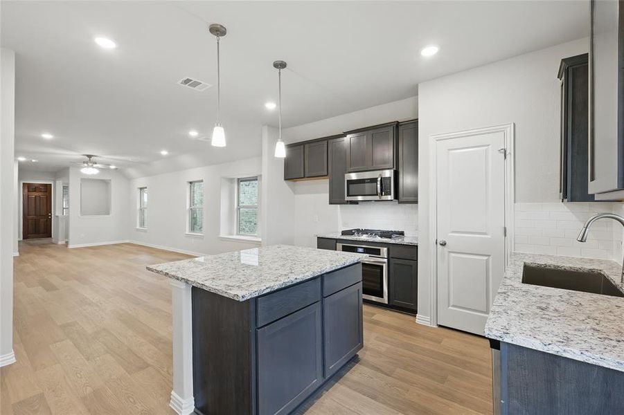 Kitchen with hanging light fixtures, light stone counters, light wood-style floors, appliances with stainless steel finishes, and recessed lighting