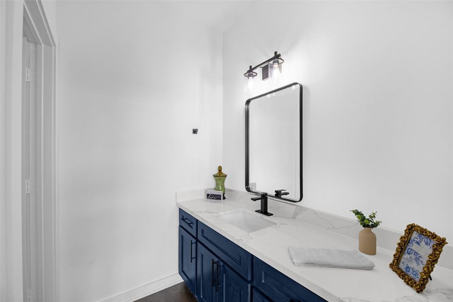 Contemporary bathroom with a sleek white countertop, a black-framed mirror, and deep blue cabinetry.
