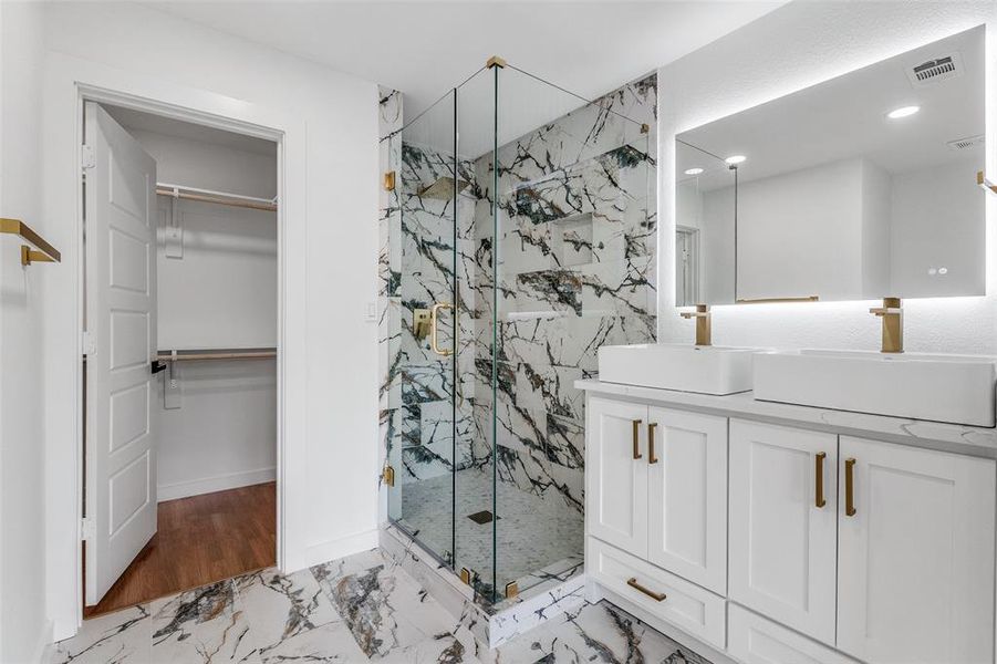 Full bathroom featuring a spacious closet, a marble finish shower, double vanity, and light marble finish flooring Full bathroom featuring a spacious closet, a marble finish shower, double vanity, and light marble finish flooring