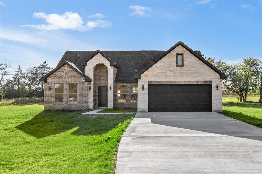 French country home with a front lawn, driveway, stone siding, and brick siding