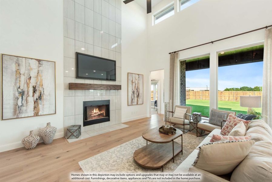 Living room with two-story tiled fireplace, hardwood floors, and large windows overlooking backyard