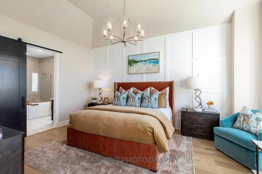 Bedroom with a barn door, a decorative wall, a chandelier, wood finished floors, and ensuite bath