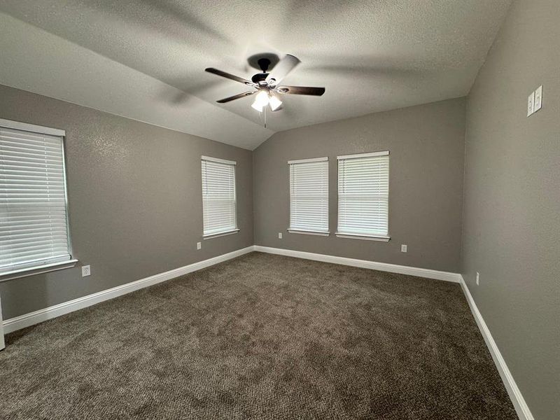 Carpeted empty room with a textured ceiling, ceiling fan, and lofted ceiling