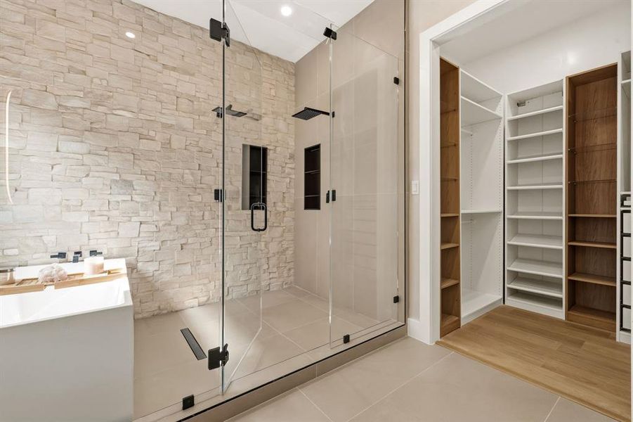 Walk-in shower with clear glass enclosure and black hardware, featuring a stone accent wall and built-in shelving