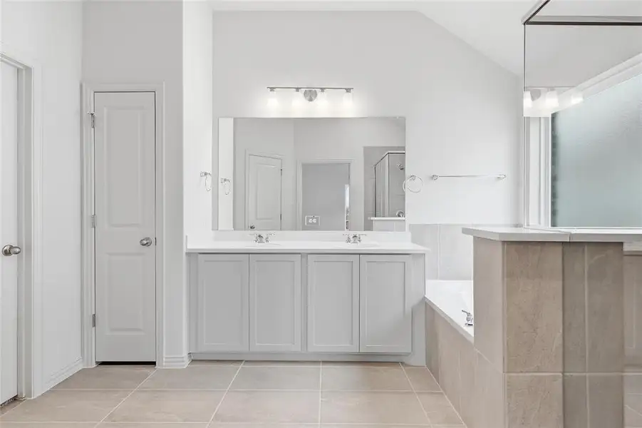 Bathroom with double vanity, a shower stall, light tile patterned floors, a garden tub, and lofted ceiling