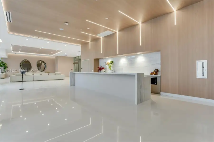 Modern lobby featuring high-gloss tile flooring, floor-to-ceiling wood-finish wall paneling, linear recessed lighting, and a stone-topped reception desk with integrated backsplash