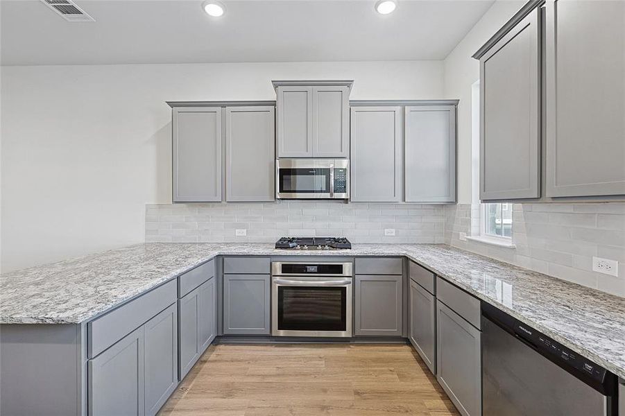 Kitchen with gray cabinetry, a peninsula, stainless steel appliances, light wood-style flooring, and recessed lighting