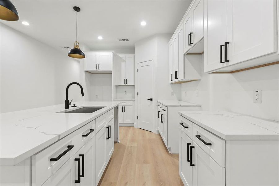 Kitchen featuring light stone countertops, light wood finished floors, recessed lighting, a kitchen island with sink, and white cabinetry Kitchen featuring light stone countertops, light wood finished floors, recessed lighting, a kitchen island with sink, and white cabinetry