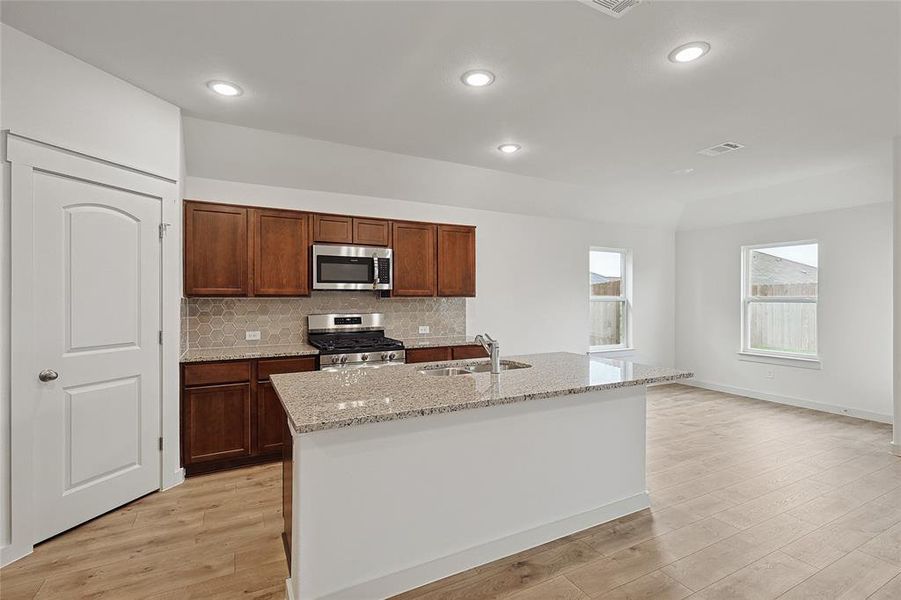 Kitchen with light stone counters, stainless steel appliances, light wood-type flooring, and an island with sink