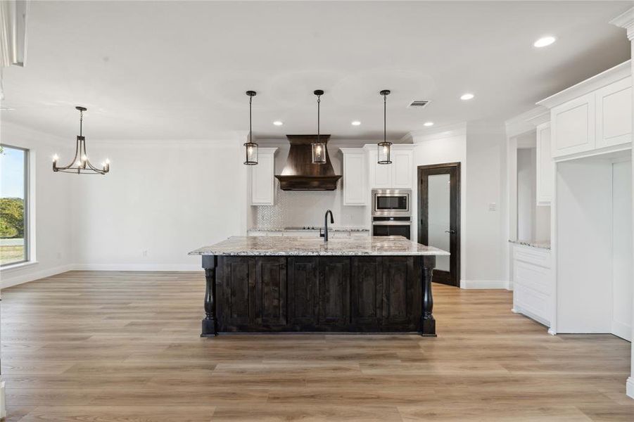 Kitchen with white cabinets, premium range hood, light hardwood / wood-style floors, light stone countertops, and appliances with stainless steel finishes