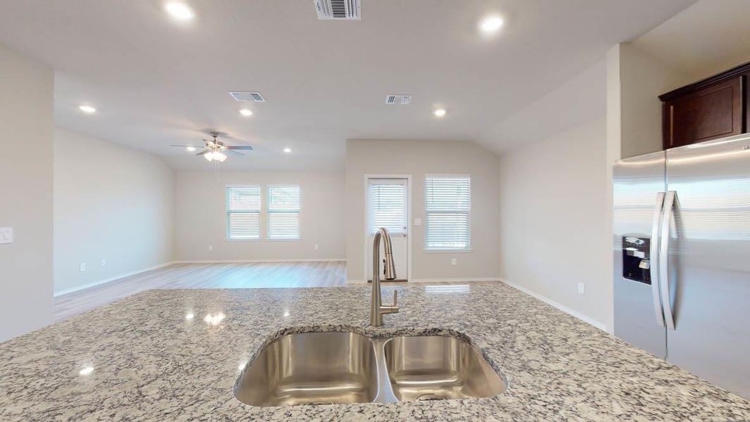 Kitchen featuring stainless steel refrigerator with ice dispenser, light stone countertops, recessed lighting, vaulted ceiling, and open floor plan