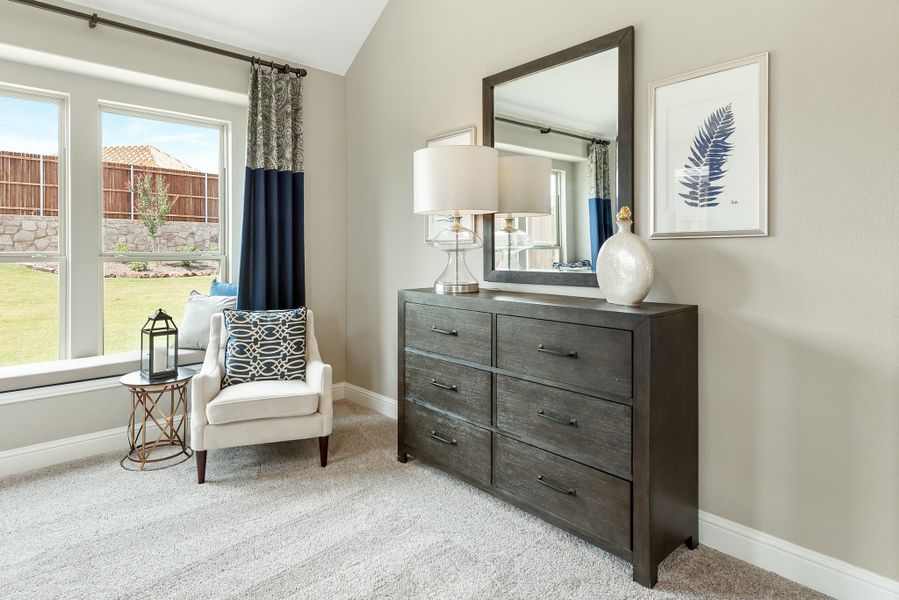 Bedroom with dark wood dresser and mirror, white accent chair, carpet flooring, and large windows with blue curtains